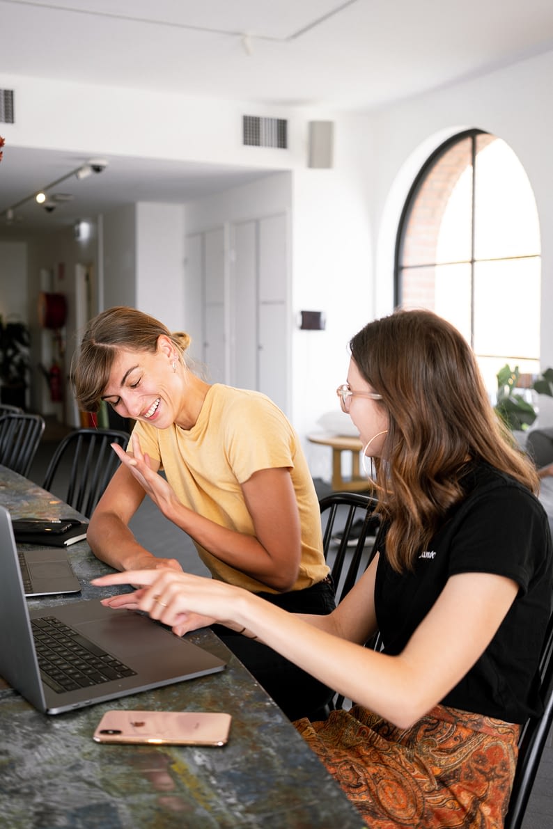 boss and employee sitting on same side of desk looking at a laptop together